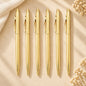 Set of six slim gold ballpoint pens with matching gold clips arranged on a warm beige background.