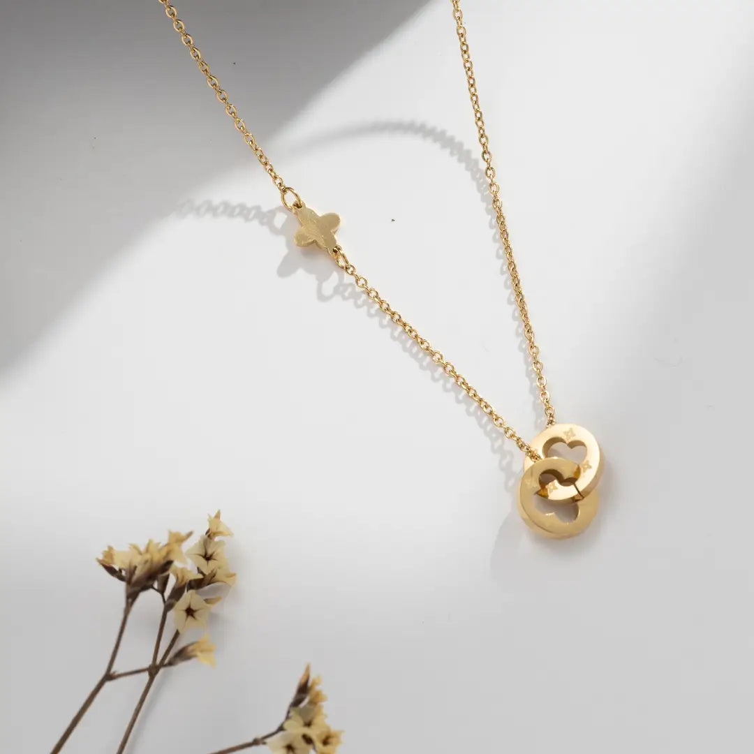 Gold necklace with double heart pendant and small butterfly detail on the chain, displayed on a soft neutral background.