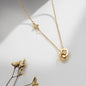 Gold necklace with double heart pendant and small butterfly detail on the chain, displayed on a soft neutral background.