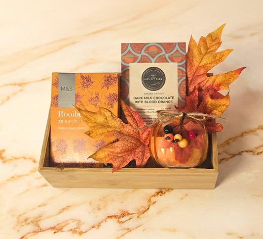 M&S Autumn Delights Gourmet Tray featuring M&S Rooibos Tea, M&S Dark Milk Chocolate with Blood Orange, and a small autumn-themed candle in a wooden tray.