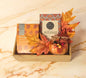 M&S Autumn Delights Gourmet Tray featuring M&S Rooibos Tea, M&S Dark Milk Chocolate with Blood Orange, and a small autumn-themed candle in a wooden tray.