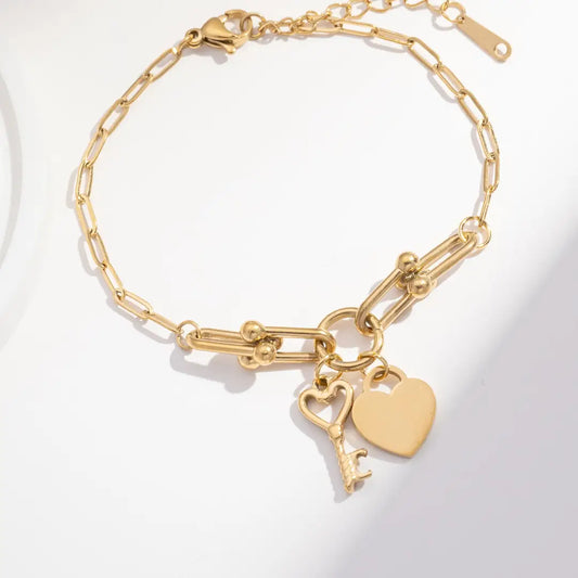 Gold chain bracelet with heart and key charms, featuring a modern link design on a light background.