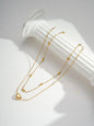 Layered gold necklace with delicate chains, small bead accents, and a heart pendant displayed on a white decorative stand.