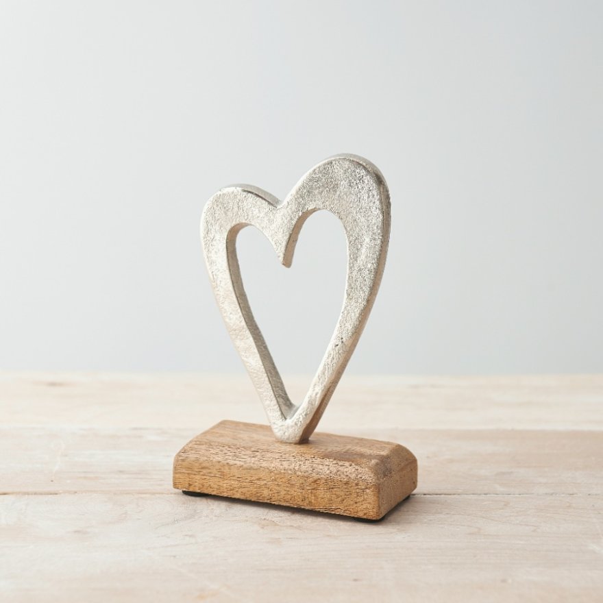 Abstract metallic heart ornament mounted on a wooden base, minimalist decorative piece on a light wooden surface.