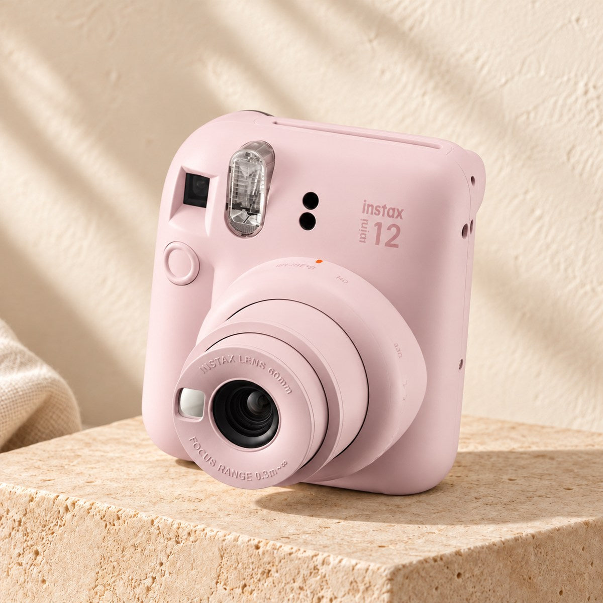 Fujifilm Instax Mini 12 in blossom pink on a beige stone display with an ivory boho background.