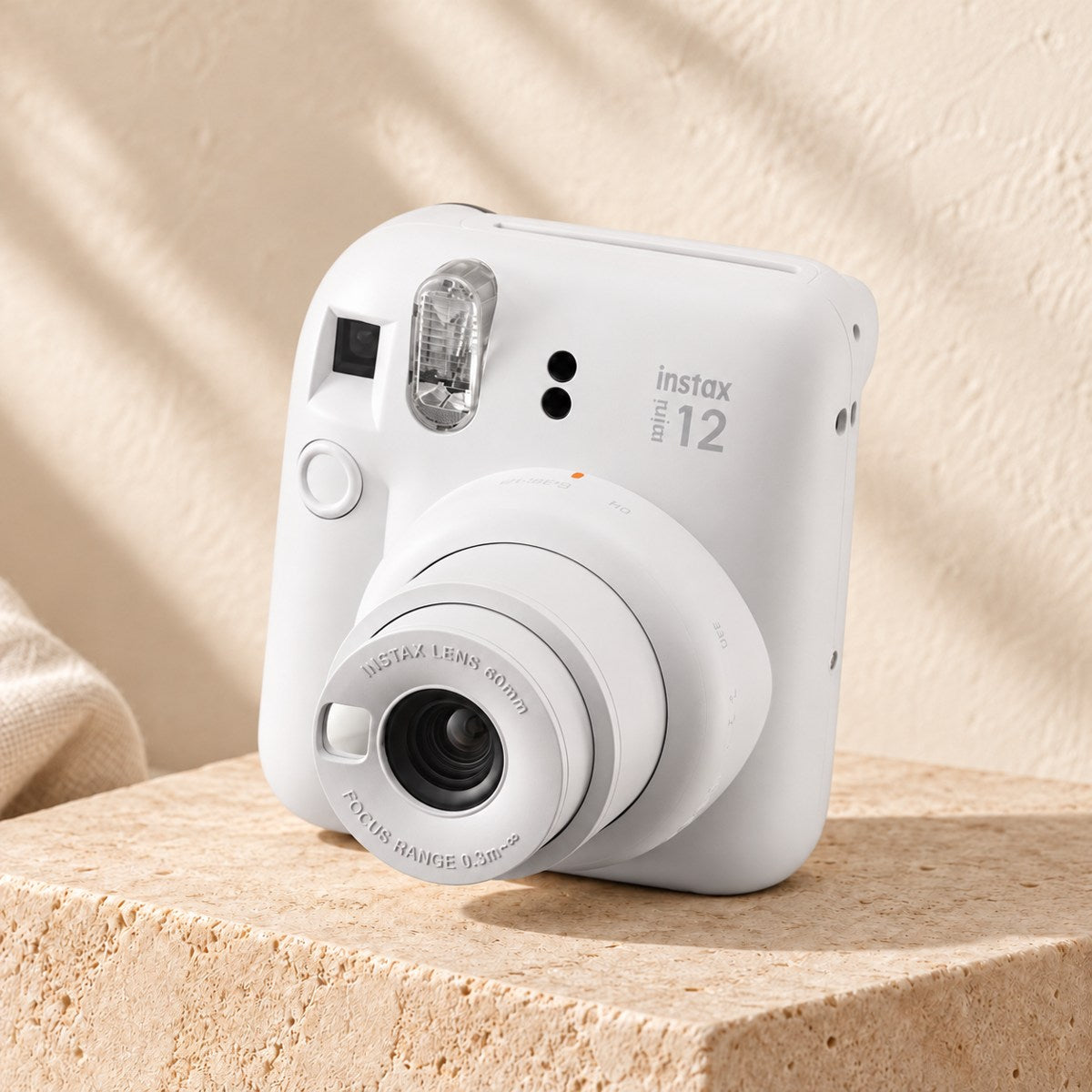 Fujifilm Instax Mini 12 in clay white on a beige stone display with an ivory boho background.
