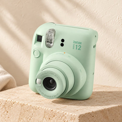Fujifilm Instax Mini 12 in mint green on a beige stone display with an ivory boho background.