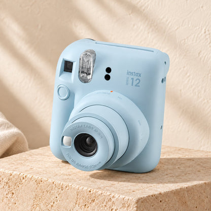 Fujifilm Instax Mini 12 in pastel blue on a beige stone display with an ivory boho background.