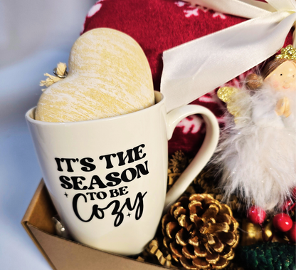 The 'Season to be Cozy' Christmas gift box with a red plush blanket, fuzzy reindeer socks, heart-handled mug, Sandalwood diffuser, and angel ornament.