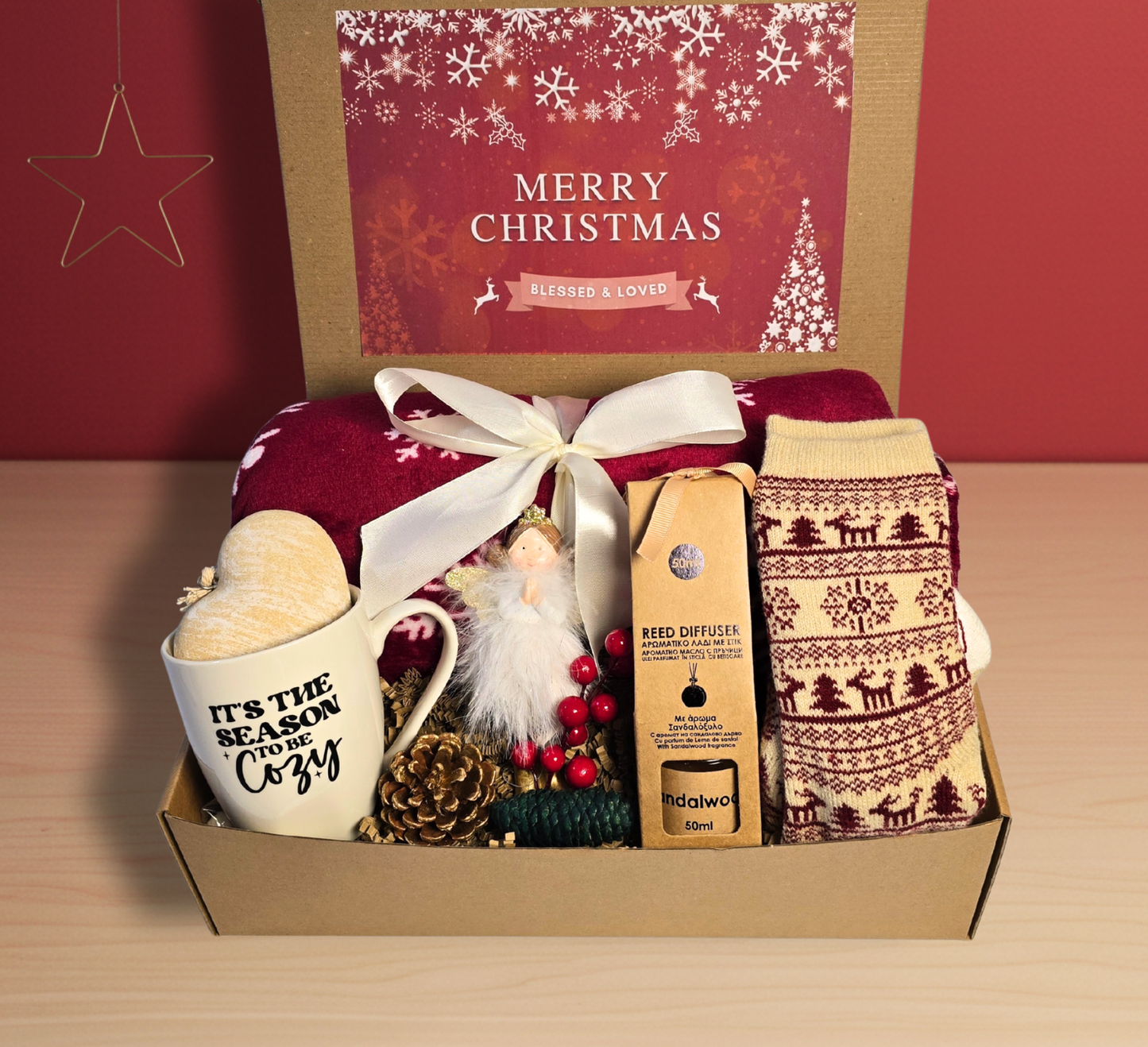 The 'Season to be Cozy' Christmas gift box with a red plush blanket, fuzzy reindeer socks, heart-handled mug, Sandalwood diffuser, and angel ornament.