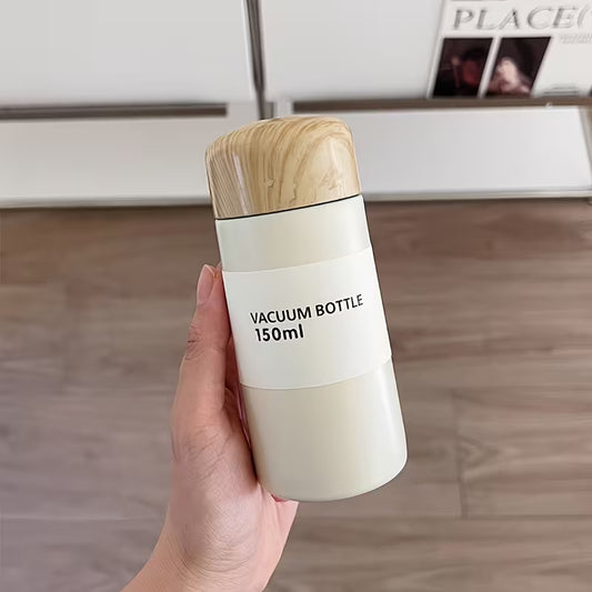 Minimalist 150ml vacuum bottle with wood-style lid and insulated thermal design, held in hand on a neutral background.