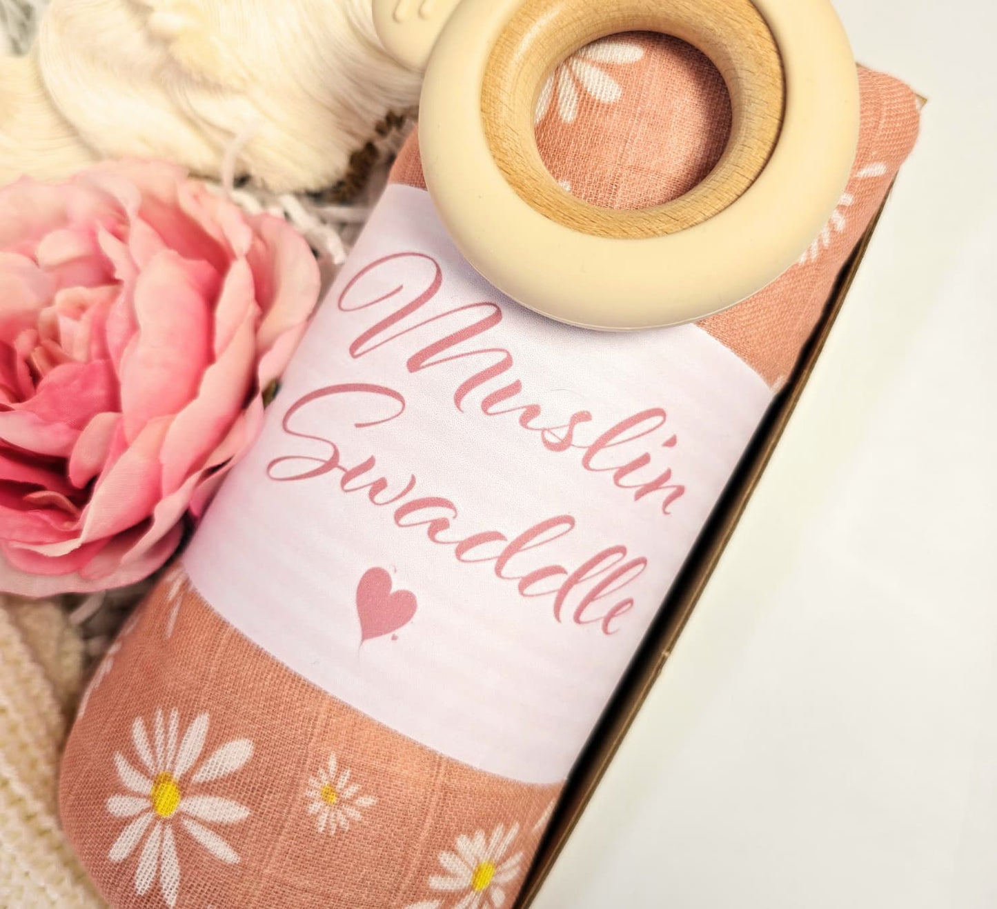 Newborn Baby Girl gift set featuring a 'Just Arrived' knitted sweater, pink daisy muslin swaddle, wood teether, plush bunny toy, and macrame rainbow.