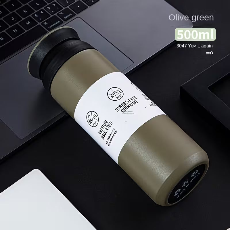 Olive green 500ml stainless steel thermal bottle with white sleeve label displayed on a desk beside a laptop.