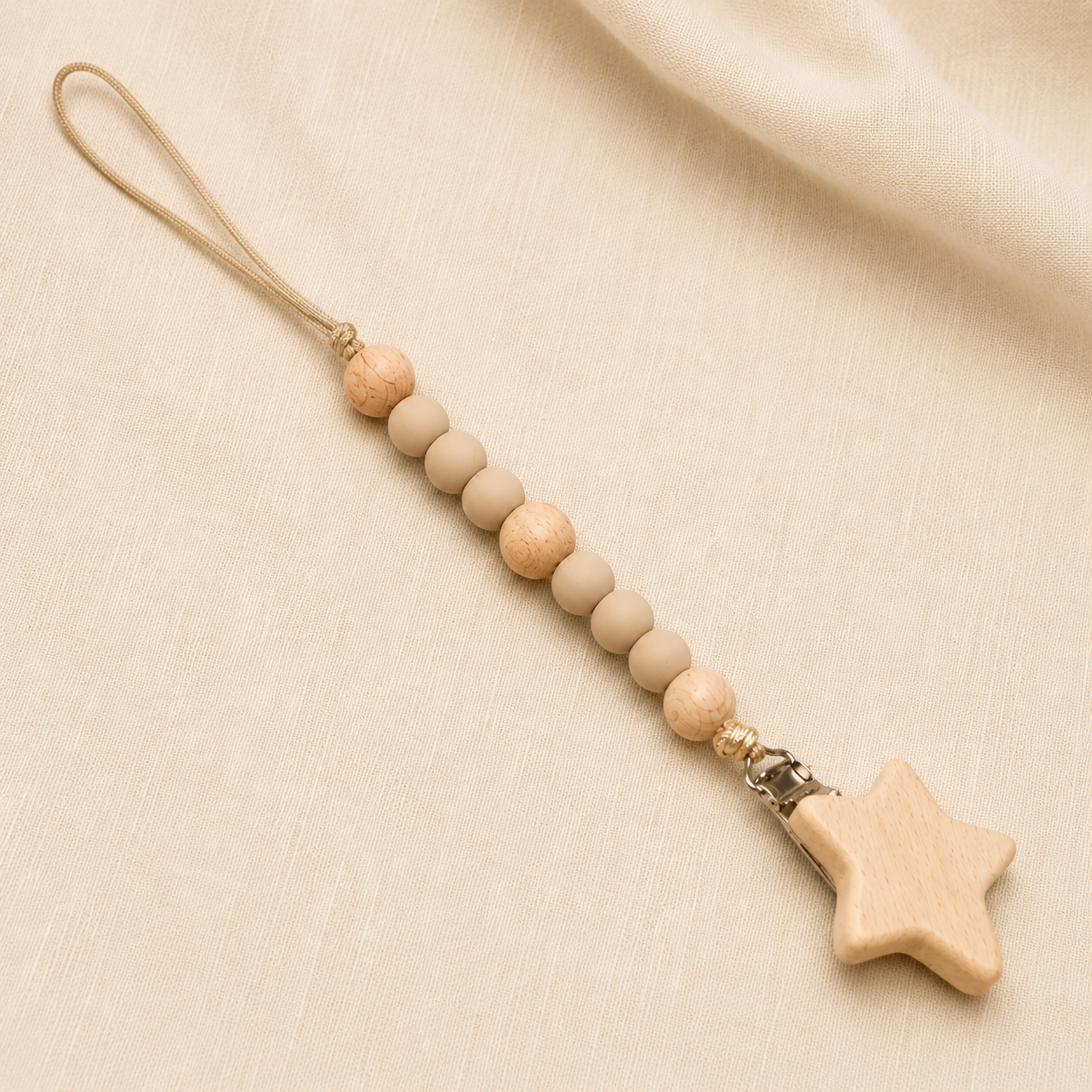 Beige and natural wooden bead pacifier clip with wooden star on cream fabric.