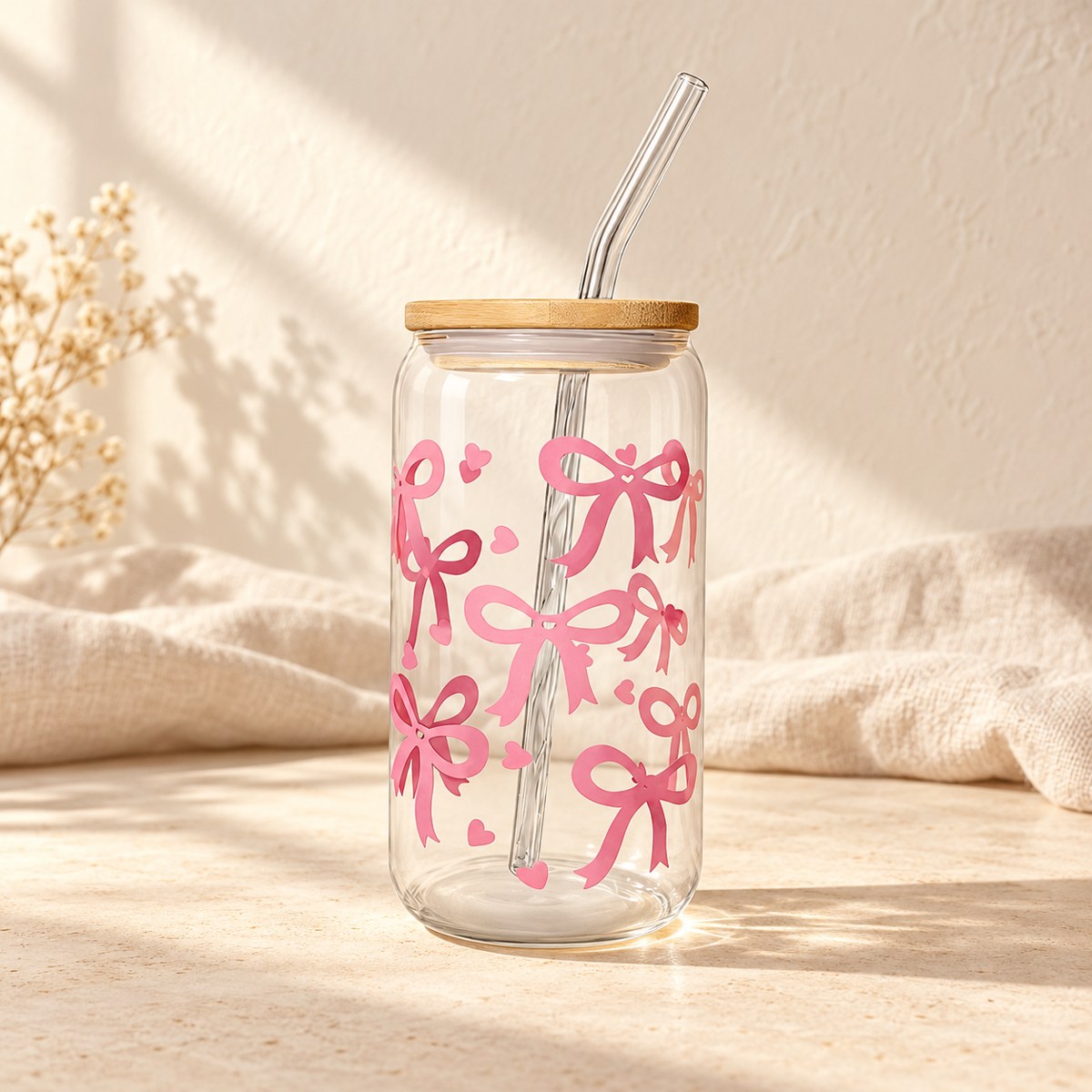 Clear drinking glass decorated with pink bows and hearts, with a bamboo lid and transparent bent straw.