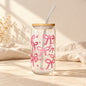 Clear drinking glass decorated with pink bows and hearts, with a bamboo lid and transparent bent straw.