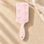 Back of a pale pink paddle hairbrush decorated with pink bows and hearts, with a hanging hole in the handle.