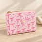 Pale pink wallet with bow and heart print, gold-tone snap tab, zipped pocket and wrist strap.