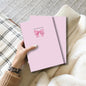 Cute pink notebook with elegant bow design and feminine aesthetic displayed on a neutral background.