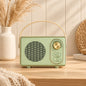 Retro portable speaker with gold-tone dial and carry handle, available in cream, sage green, blush pink and lilac.