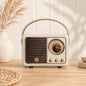 Retro portable speaker with gold-tone dial and carry handle, available in cream, sage green, blush pink and lilac.