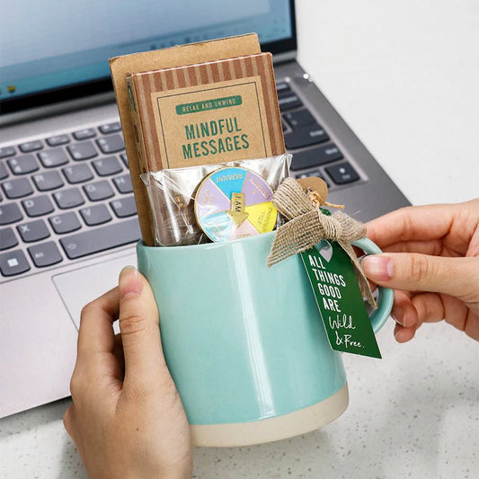 Ceramic mug gift set featuring mindful messages cards, affirmation spinner, inspirational tag, and wellness keepsakes, beautifully styled in a cozy setting with soft lighting, candle, and neutral décor.