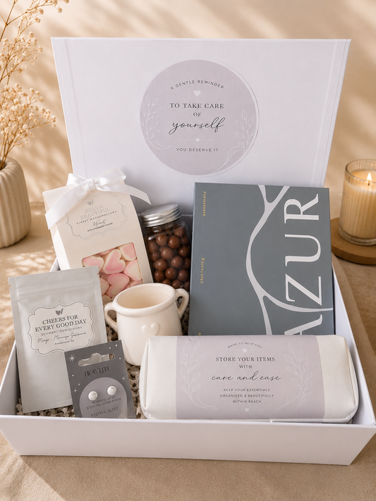 Luxury self-care gift box featuring marshmallows, chocolate treats, bath salts, ceramic mug, sterling silver earrings, wellness journal, and storage pouch in elegant gift packaging.