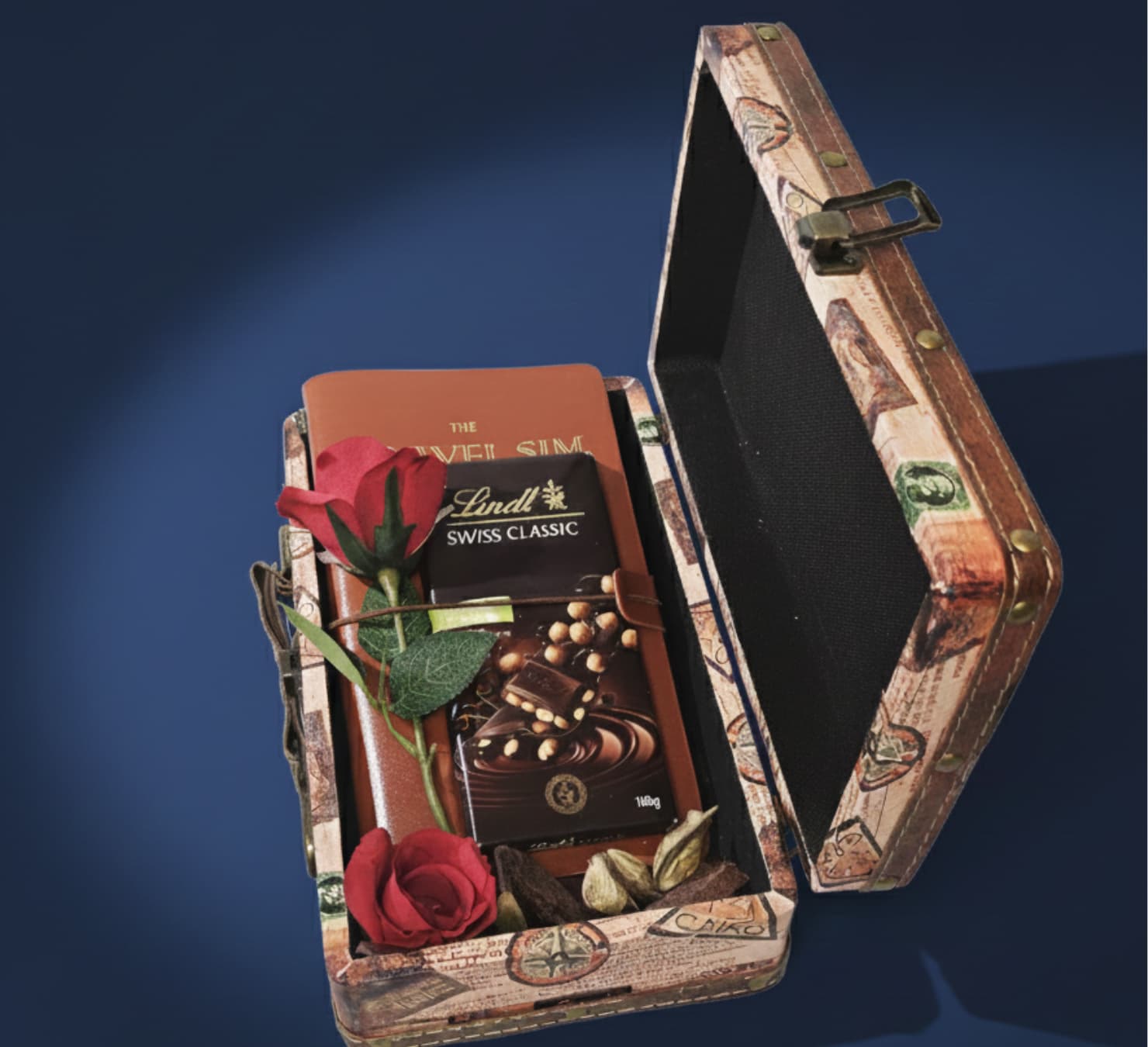 Vintage suitcase travel gift box containing a Lindt Swiss Classic chocolate bar, travel planner/sim book, and red artificial rose.