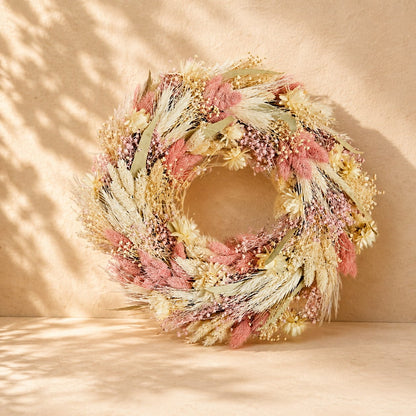 Luxury gift basket featuring a dried floral wreath, pink ceramic mug, wooden house keepsake, marshmallow gift box, and decorative home plaque arranged in a woven basket with a pink ribbon.