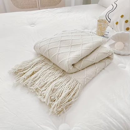 Cream diamond knit throw blanket with tassel fringe folded on a bed, cozy luxury home décor accessory.