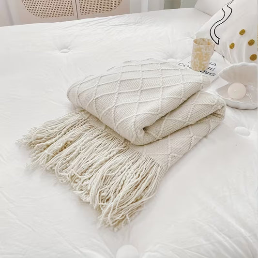 Cream diamond knit throw blanket with tassel fringe folded on a bed, cozy luxury home décor accessory.