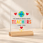 Clear acrylic plaque reading The World Needs More Teachers Like You, with a smiling globe, red hearts and yellow stars on a wooden stand.