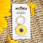 Yellow sunflower enamel keyring with “You are my sunshine” message on packaging, placed on a woven surface with sunflower petals.
